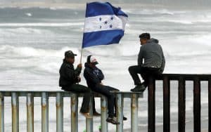 Gente sostiene una bandera hondureña mientras están sentados en la valla fronteriza entre México y Estados Unidos en Tijuana, México, el 29 de abril.(CNS/México).