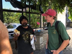 El Misionero Laico Maryknoll Tim Ross conversa y le ofrece algo de comer a Louis, un indigente que vive en la intemperie, cerca a un hospital en el centro de San Salvador, El Salvador.
