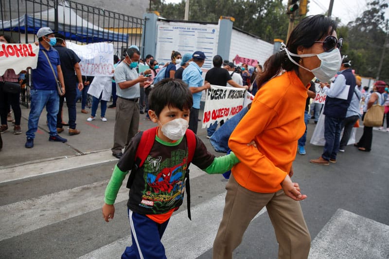 Una mujer y un niño son vistos frente a trabajadores de salud que protestan por la falta de suministros médicos adecuados a principios de mayo frente a un hospital en Lima, Perú, durante la pandemia de COVID-19. (Foto del CNS / Sebastian Castaneda, Reuters)