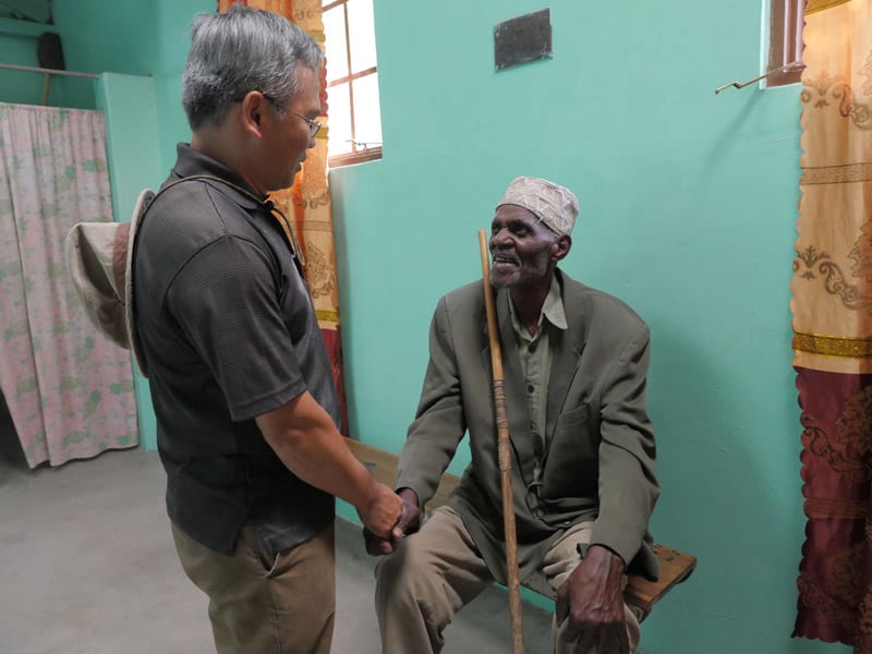 El misionero Maryknoll saluda a un hombre en la clínica de la parroquia de Ndoleleji. (Sean Sprague/Tanzania)