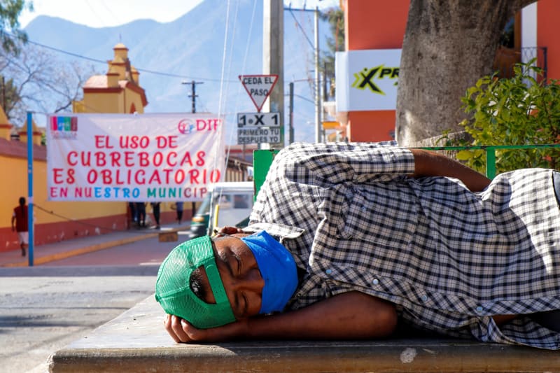 Un hombre con mascarilla duerme en un parque de Tlacolula de Matamoros, México, el 30 de enero de 2021, cerca de una pancarta que dice "El uso de mascarillas es obligatorio en nuestro municipio", durante la pandemia de coronavirus. (Foto del CNS / Jorge Luis Plata, Reuters)