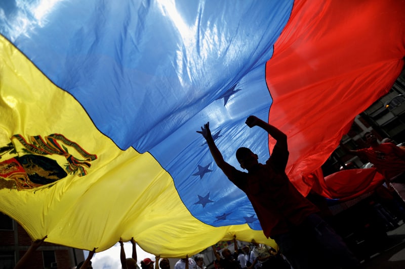 Los partidarios del presidente Nicolás Maduro sostienen una bandera de Venezuela durante un mitin en Caracas el 14 de agosto de 2017. La administración Biden anunció el 8 de marzo de 2021 que ofrecerá 18 meses de Estatus de Protección Temporal a unos 320.000 venezolanos en los EE. colapso económico. (CNS/Ueslei Marcelino, Reuters)