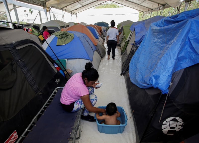 Una mujer migrante baÒa a su hijo fuera de su tienda de campaÒa en un campamento de migrantes en Matamoros, MÈxico, el 30 de abril de 2020. Personas buscando asilo en Estados Unidos contin˙an viviendo en el campamento pero muchos han dicho que tienen miedo de seguir allÌ por todos los percances y la amenaza de la violencia a manos de carteles que controlan la frontera. (Foto CNS/Daniel Becerril, Reuters)