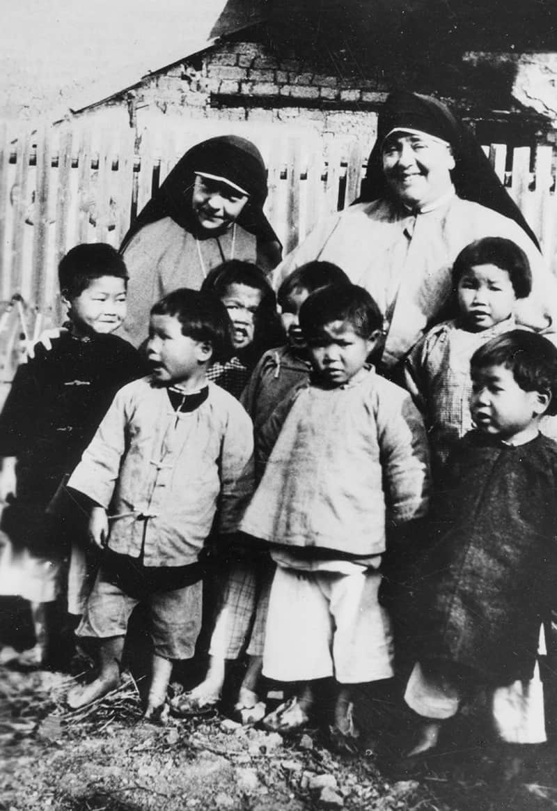 La Hna. Paul McKenna (izq.) y la Madre Mary Joseph sonríen con niños en China en 1926.