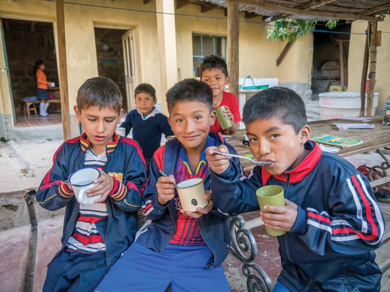Niños que asisten al programa de tutoría después de la escuela disfrutan de un nutritivo refrigerio de avena y leche, preparado por la misionera Nguyen en la casa parroquial deTacopaya. (Nile Sprague/Bolivia)