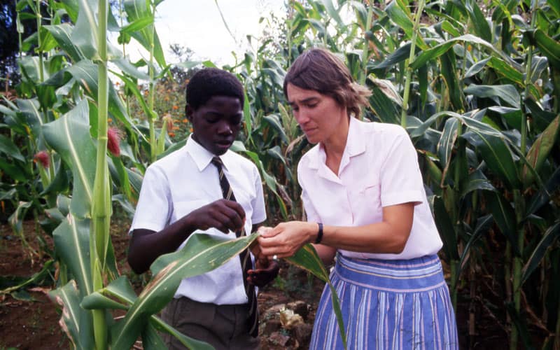 La hermana Miller, capacitada en agricultura y cría de animales en Gweru Teachers College en Zimbabwe, habla sobre técnicas agrícolas con un estudiante en 1988. (Maryknoll Mission Archives)