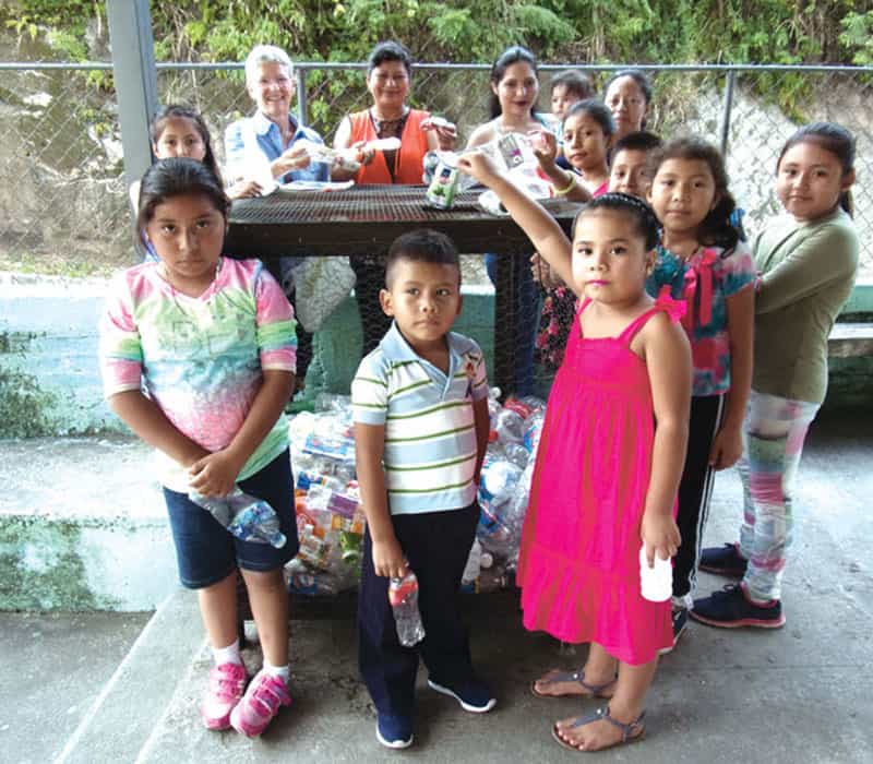 pastoral de la tierra en el Salvador: La misionera laica Maryknoll Margaret Vámosy y líderes comunitarios adultos enseñan a los niños del pueblo de San Nicolás a reciclar botellas en 2018. (Cortesía de Margaret Vámosy/El Salvador)
