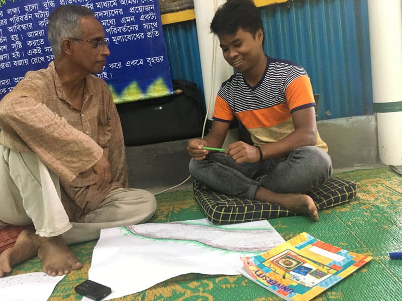 Merwyn De Mello escucha mientras un voluntario de L'Arche comparte su río de vida. Los De Mellos facilitaron varias sesiones sobre la concientización sobre el trauma para los voluntarios de L'Arche en Mymensingh, Bangladesh en 2019. (Cortesía de Maryknoll Lay Missioners)