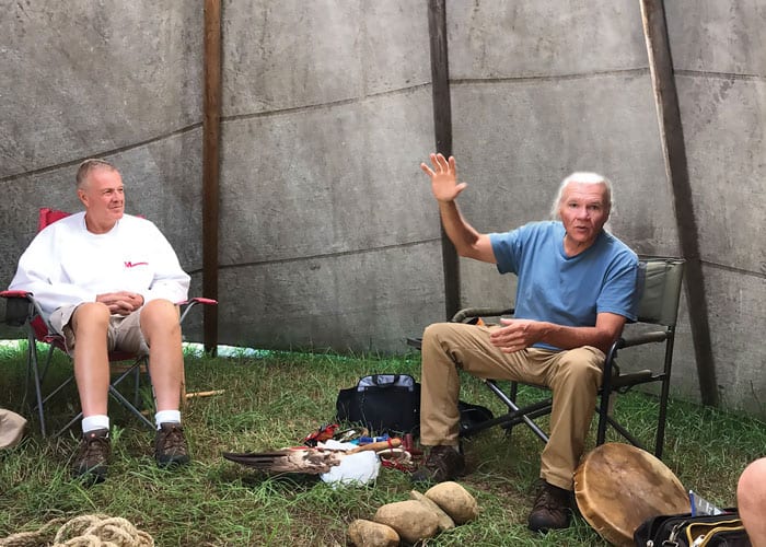 Dentro de la carpa de nativos americanos, el Diácono Dennis Holley (izquierda), quien ayudó a organizar el viaje de inmersión, escucha junto a otros participantes al jefe Gary Cheeseman que cuenta la historia de la creación de los lakota. (Scott Giblin/EE.UU.)