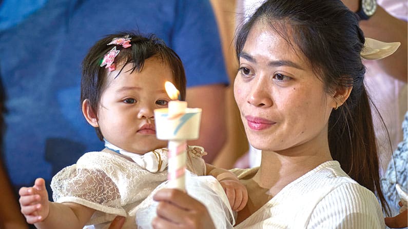 Sosteniendo una vela, una trabajadora migrante, Alina Querubin, alza a su hija, Hsin Yi Zoa, tras el bautizo de la pequeña en la Iglesia Católica Tanzi en Taichung, Taiwán. (Paul Jeffrey/Taiwan)