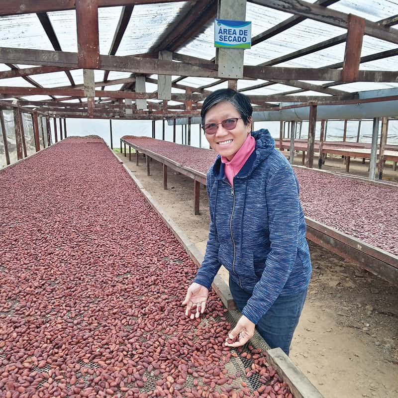 La misionera inspecciona granos de cacao secándose al aire libre en una granja colectiva. (Cortesía de Esperanza Principio/Perú)