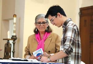Sisolak, hijo de un misionero laico, firma el convenio para servir en el extranjero con los Misioneros Laicos Maryknoll ante Elvira Ramírez, directora ejecutiva de los Misioneros Laicos Maryknoll. (Andrea Moreno-Díaz/EE.UU.)