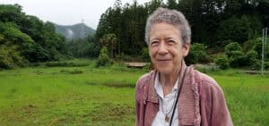 Imagen destacada: En una visita a la "zona muerta" de Fukushima que fue gravemente afectada por la radiación de explosiones de los reactores nucleares Daiichi y Daini de Fukushima, la Hermana Maryknoll Kathleen Reiley posa en un arrozal cuya capa vegetal fue retirada por la alta radioactividad. (Sean Sprague/Japón)