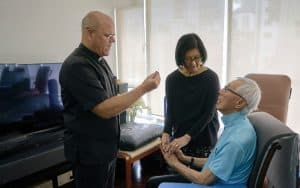 El Padre Maryknoll Joseph Everson lleva la Sagrada Comunión a Linda y Pedro Ching a su hogar. Pedro, quien padece la enfermedad de Parkinson, tiene dificultades para asistir a la Misa en la iglesia. (Paul Jeffrey/Hong Kong)