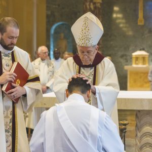 El prelado ordenante, Obispo Seitz, impone las manos sobre Matthew Sim, quien fue ordenado sacerdote con Patrick Okok el 7 de junio. (Octavio Durán, OFM/EE.UU.)