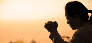 Silueta de una mujer orando a Dios con un atardecer de fondo. (Adobe Stock)