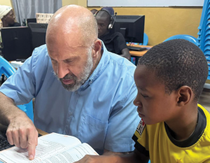 Misionero laico Maryknoll Richard Tarro ayuda a un niño con sus tareas en su misión en Kenia. (Cortesía de Richard Tarro/Kenia)