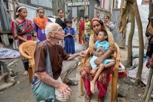 El Padre Maryknoll Robert McCahill visita a Jair, de 8 años, y a su abuela, Rohima, en la aldea de Batabhog, cerca de Srinagar. El Padre McCahill lleva cinco décadas en Bangladesh ayudando a familias pobres a acceder a atención médica para niños con discapacidades. (Paul Jeffrey/Bangladesh)