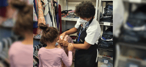 Foto de la hermana Genie Natividad ayudando a un niño migrante en la sala de ropa de Casa Alitas Welcome Center.
