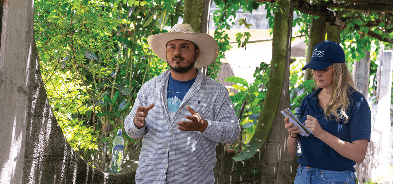 Brandon explica cómo obtuvo apoyo de trabajadores locales de CRS, como Jessica (a la dcha.), para crear su propio huerto y generar ingresos. (Jeffrey Keller/Guatemala) 