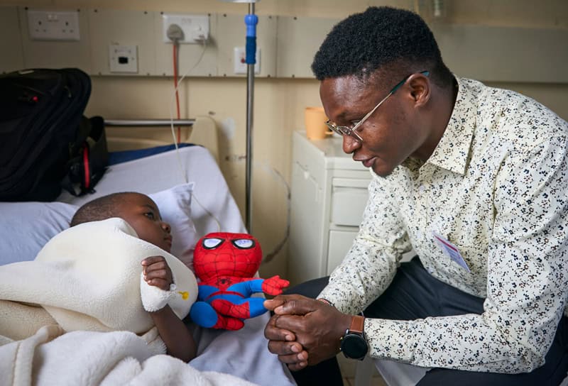 El candidato Alois Simpilisi visita a un niño en el hospital St. Francis Community en Nairobi, Kenia, donde es capellán como parte de su ministerio pastoral y de discernimiento. (Paul Jeffrey/Tanzania)